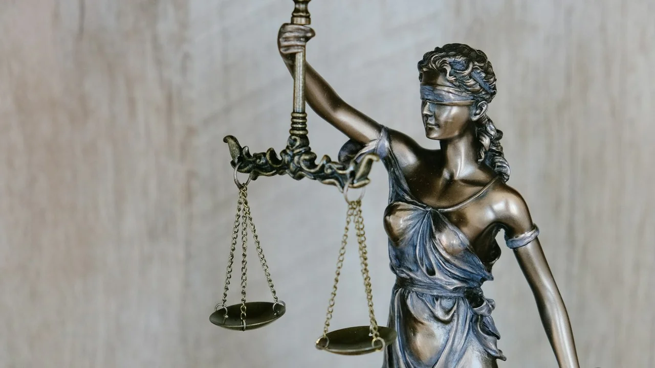 Close-up of a bronze Lady Justice statue holding balanced scales, a photographic news thumbnail for the Supreme Court SAVE database stay