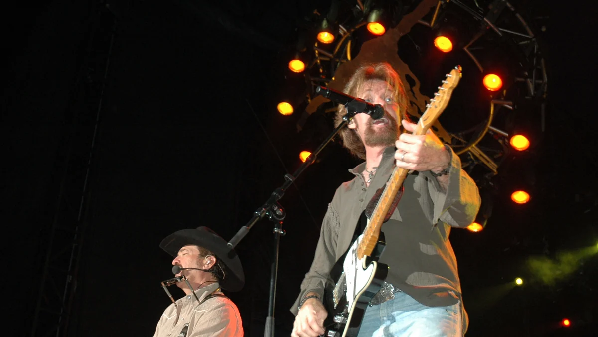 Ronnie Dunn sings and plays electric guitar beside Kix Brooks in a black cowboy hat under orange stage lights at a 2009 Brooks & Dunn concert