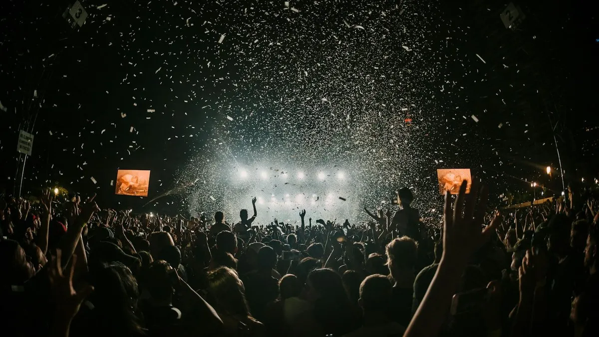 Outdoor night festival crowd facing a brightly lit stage with confetti